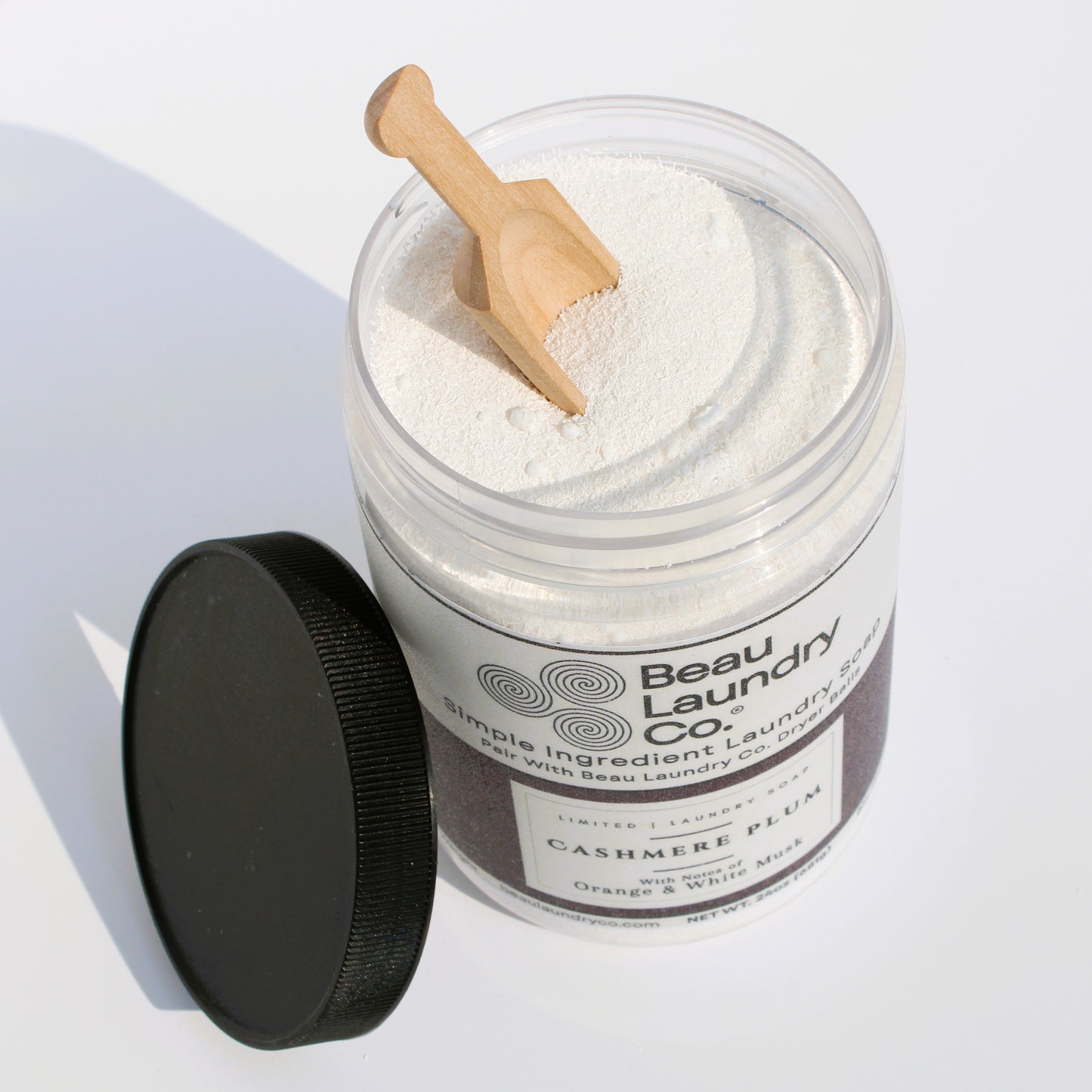 Beau Laundry Co. laundry detergent in a jar with a wooden scoop on a white background