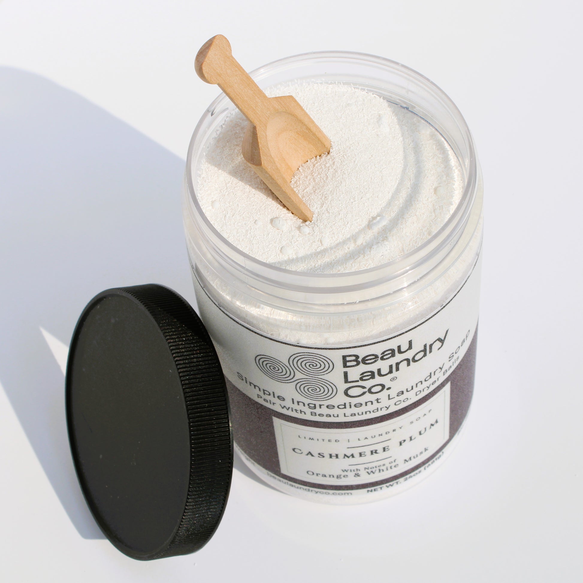 Beau Laundry Co. laundry detergent in a jar with a wooden scoop on a white background