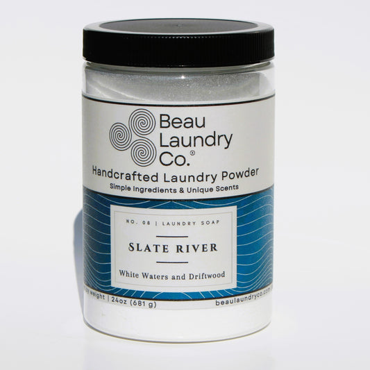 A clear plastic container of BEAU LAUNDRY CO. handcrafted laundry powder, labeled Slate River 